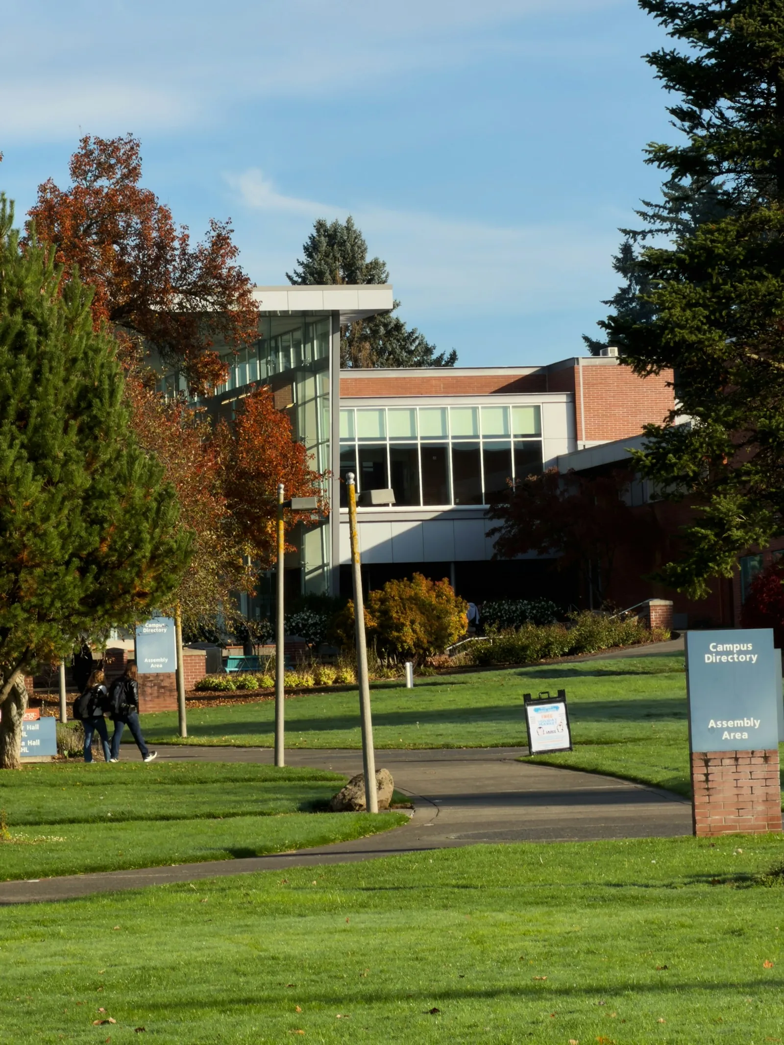 An academic building beside a green campus lawn, mature trees, and a pedestrian path