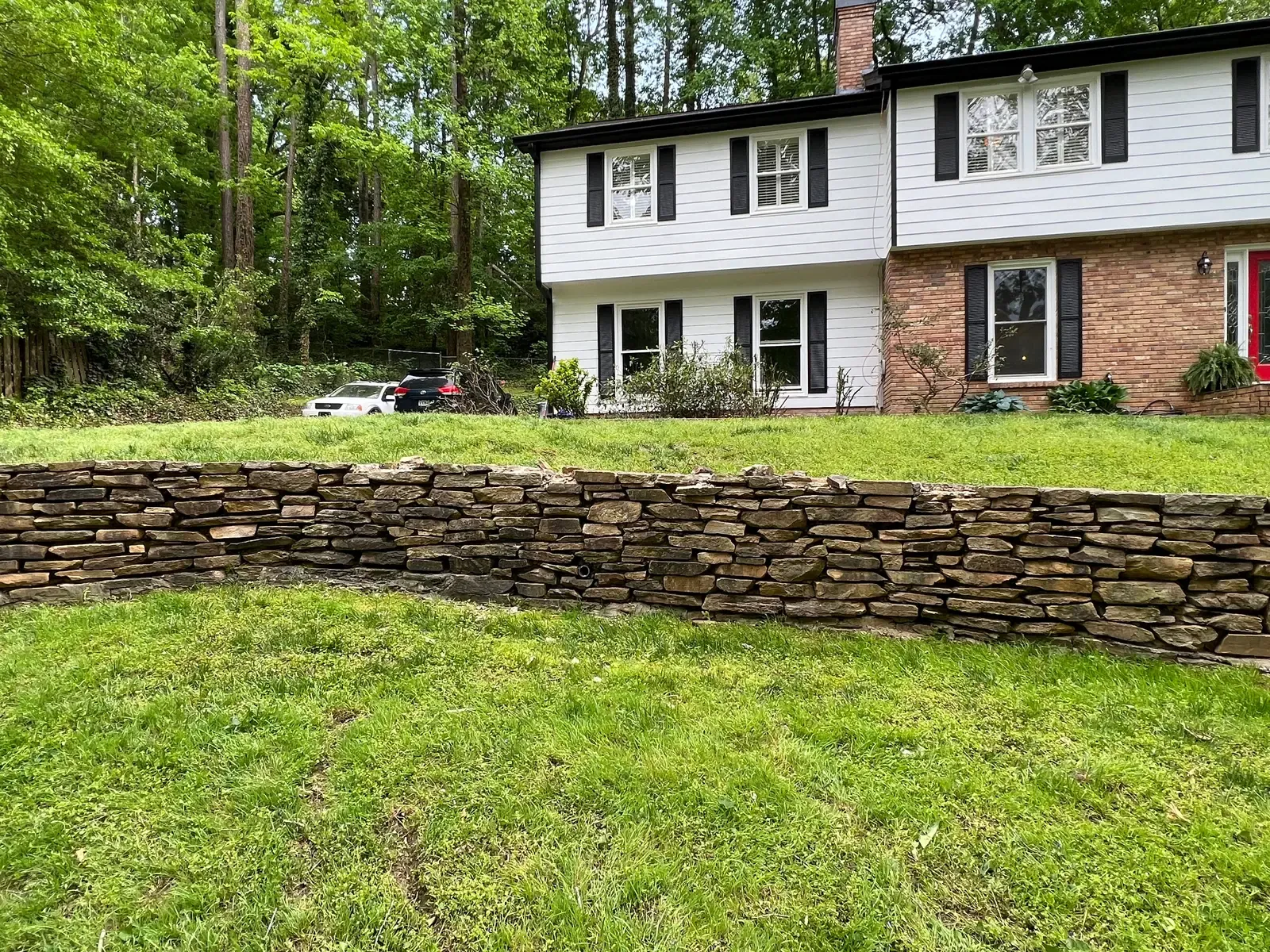 A residential property with mature trees, lawn, and a landscaped retaining wall